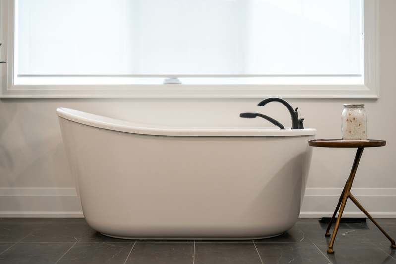 Modern freestanding bathtub in a bright, minimalist bathroom with natural light and wood accents